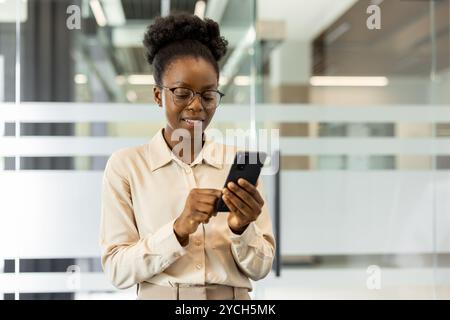 African American businesswoman using phone in modern office. Professional woman engaged and focused on smartphone, highlighting technology in daily work life. Represents connection and productivity. Stock Photo