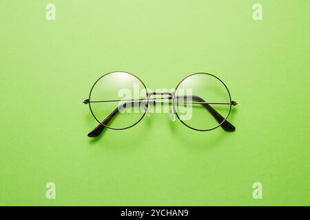 Glasses in round thin metal frame isolated on green surface. Stock Photo