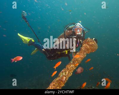 A female scuba diver holds on to an old Spanish anchor at the canyons, Puerto Galera, Philippines. This can be a very challenging dive with a strong current. Down currents are common in the area Stock Photo