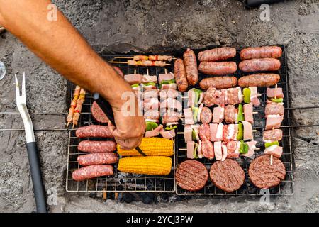 Various meats and vegetables cooking on outdoor barbecue grill. Fresh sausages, hamburgers, corn and kebabs being prepared during summer cookout Stock Photo