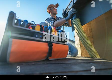 A person is performing maintenance on a roof, utilizing tools laid out in an organized manner beside them under a clear blue sky. Stock Photo