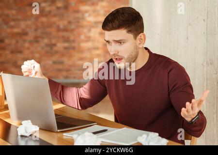 Emotional Worker Looking At Laptop Having Problem Sitting In Office Stock Photo