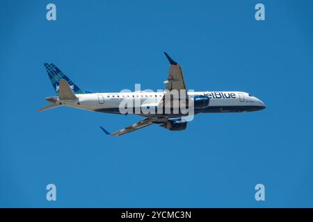 A JetBlue Embraer 190 airliner gains altitude shortly after takeoff in a deep blue sky. Stock Photo