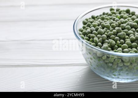 Frozen green peas in glass bowl on white wooden table, closeup. Space for text Stock Photo