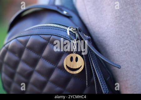 Woman with wooden keychain in shape of smiley face and black leather decor on her backpack outdoors, closeup. Selective focus Stock Photo