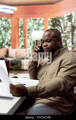 Entrepreneur sharing office space layout ideas with designers on phone call, planning a building renovation for the new creative workspace. Using architectural blueprints for a modern layout. Stock Photo