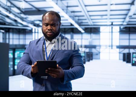 Knowledgeable programmer in server hub installing newly ordered storage units using tablet. IT specialist working in data center workspace housing storage rackmounts infrastructure Stock Photo