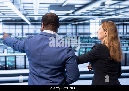 Team of engineers in server hub checking hardware after installing storage units. Teamworking colleagues in data center doing maintenance after replacing mainframes components Stock Photo