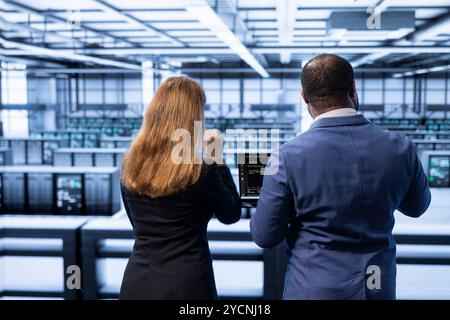 Supervisor inspecting server hub, making sure rigs are functioning optimally. Employee showing overseeing inspector recovery plan on laptop, monitoring energy consumption Stock Photo