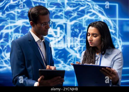 Technicians use AI cognitive computing to extract information from complex data on tablet. Employees at work using artificial intelligence technology, checking parameters Stock Photo