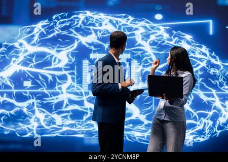 IT department coworkers solving tasks on laptop and tablet, running artificial intelligence programming scripts. Team of technicians brainstorming ways to develop AI applications Stock Photo