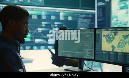 Governmental hackers analyzing data for cyber threat detection, looking at a big screen in high tech office. Highlight cyber intelligence, online security and prevention of digital threats. Camera B. Stock Photo