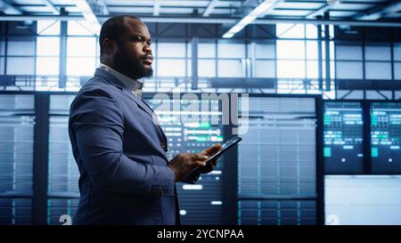 Technician walking in server room, doing checkup, inputting data on tablet of needed fixes. IT professional working in data center facility housing storage infrastructure, camera B Stock Photo
