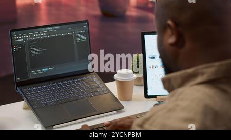 AI software developer creating an algorithm for deep learning and data mining, coding on his laptop at home office. Expert processing binary code on supercomputer neural network. Camera A. Stock Photo