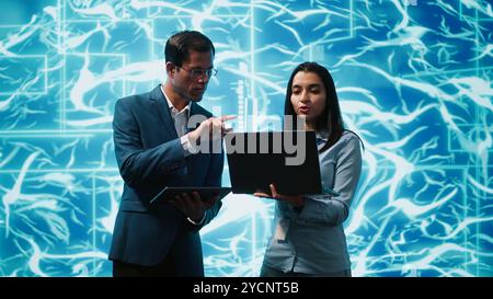 IT department colleagues solving tasks on laptop and tablet, running artificial intelligence programming scripts. Team of engineers brainstorming ways to develop AI applications, camera A Stock Photo