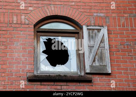 Broken window in modern empty building. Vandalised window broken double-glazed window  red brickwork wooden shutter Plastik Belfast. Stock Photo