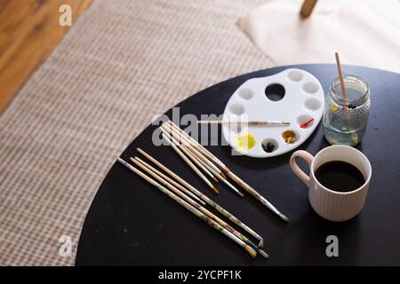 Paintbrushes and coffee on table, artist preparing for creative morning at home Stock Photo
