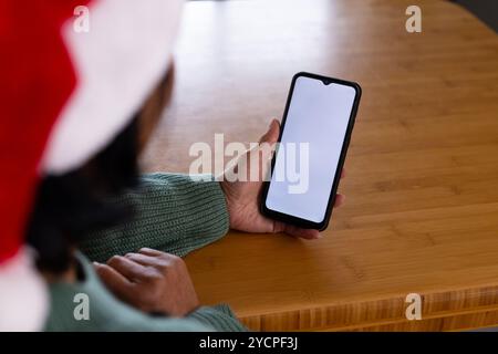 Wearing santa hat, asian senior woman holding smartphone at home during christmas, copy space Stock Photo