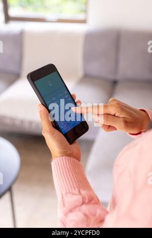 Seniro woman using smartphone app to control smart home lighting in living room Stock Photo