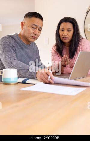 Multiracial senior couple discussing finances at home using laptop and documents Stock Photo