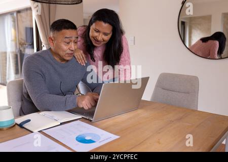 Multiracial senior couple using laptop at home, discussing finances with documents on table Stock Photo
