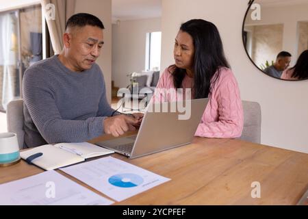 Multiracial senior couple discussing finances at home using laptop and documents on table Stock Photo