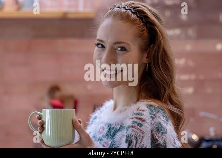At home, Smiling woman holding mug in cozy kitchen during Christmas season Stock Photo