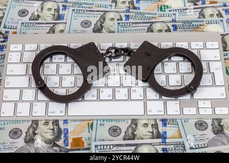 Steel handcuffs lying on a computer keyboard on the background of dollars Stock Photo