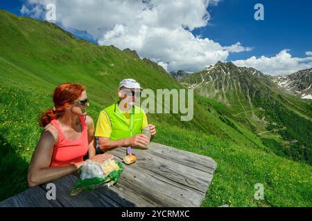 Man and woman hiking sitting on a bench and taking a break, Pfunderer Höhenweg, Zillertal Alps, South Tyrol, Italy Stock Photo