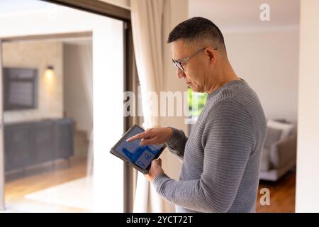 Asian senior man using tablet to control smart home system by window Stock Photo