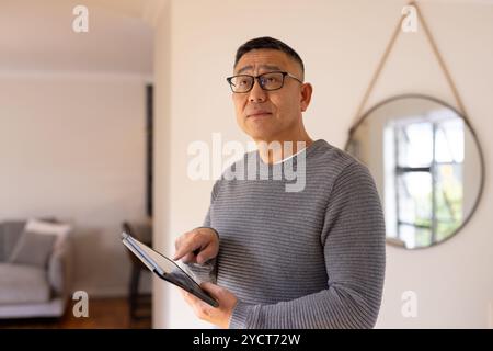 Asian senior man using tablet at home, wearing glasses, looking thoughtful and focused Stock Photo