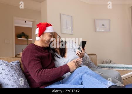 Christmas time, senior multiracial couple laughing together at home on smartphone Stock Photo
