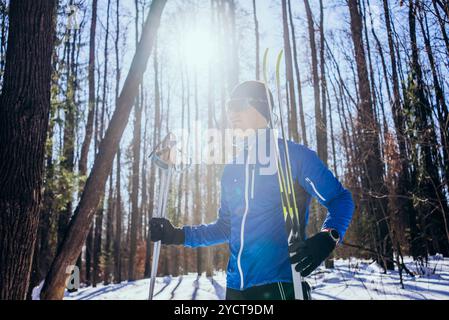 Male athlete taking a break from training, enjoying the sun shining through trees in a snowy forest, on a beautiful winter day Stock Photo