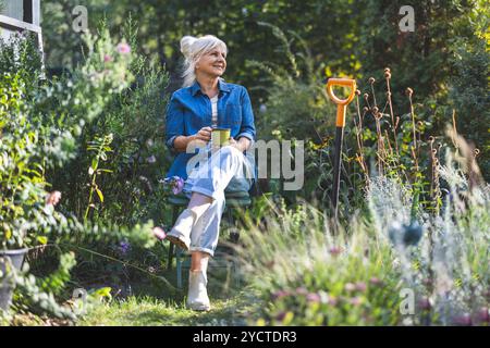 Senior woman relaxing in her garden with a cup of tea in her hand Stock Photo