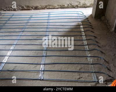 Underfloor heating system with electrical cables laid on a concrete base during installation. Stock Photo
