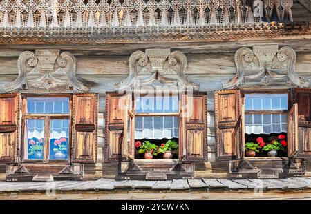 Windows of old traditional Russian log house with carved wooden trim and red geranium flowers Stock Photo