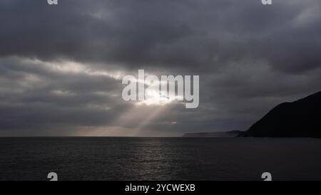 Sunbeams through stormy clouds, break in the clouds, sunbeams landing on the ocean, dark stormy day Stock Photo