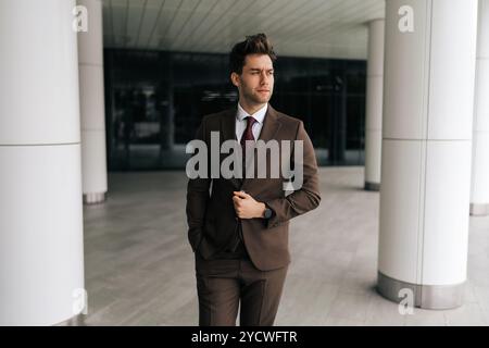 Portrait of confident successful businessman adjusting jacket while walking in modern office building, conveying sense of purpose and determination. Stock Photo