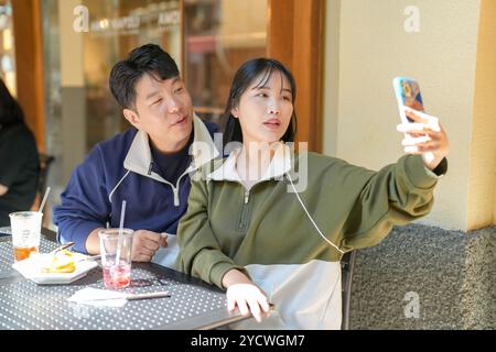 A couple, a Korean man in his 30s and a woman in her 20s, wear tracksuits and enjoy an afternoon at a nice Western-style cafe in Seoul, South Korea. Stock Photo