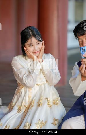 A Korean couple, a man in his 30s and a woman in her 20s, are happily wearing Hanbok and taking a selfie with a smartphone inside a historical buildin Stock Photo