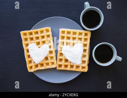 Delicious Belgian waffles with cream on a black background and two cups of coffee. Stock Photo