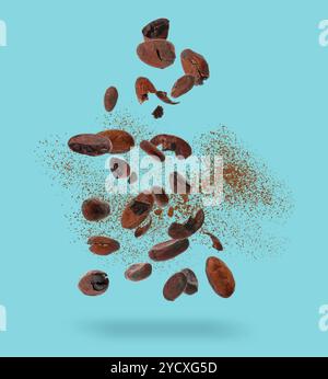 Cocoa beans and powder in air on light blue background Stock Photo