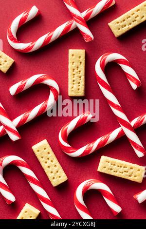 Top view of red and white striped candy canes interspersed with golden butter cookies laid out on a rich, red background. Perfect for festive holiday Stock Photo