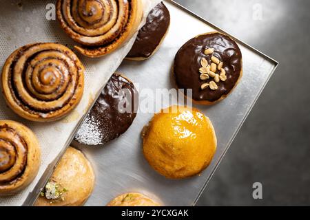 A top view of various freshly baked pastries, including cinnamon rolls, chocolate-covered donuts, and a glazed pastry Some donuts are garnished with p Stock Photo
