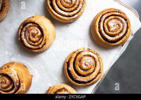 Delicious cinnamon rolls topped with a sugar icing, freshly baked and arranged neatly on a parchment-lined tray, highlighting their golden-brown textu Stock Photo