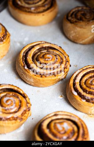 Freshly baked, golden vegan cinnamon rolls with a rich, dark filling, lightly drizzled with sugar icing, laid out on parchment paper Stock Photo