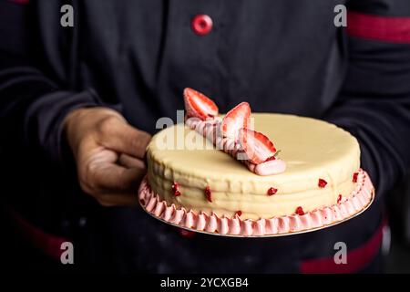 A close-up of a vegan cake decorated with white chocolate frosting, fresh strawberries, and pink cream accents The cake is elegantly presented, making Stock Photo