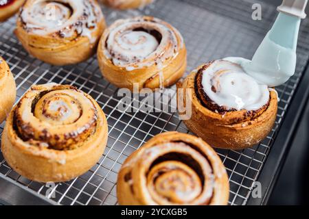Close-up view of fresh, golden cinnamon rolls with glaze being applied, sitting on a cooling rack Stock Photo