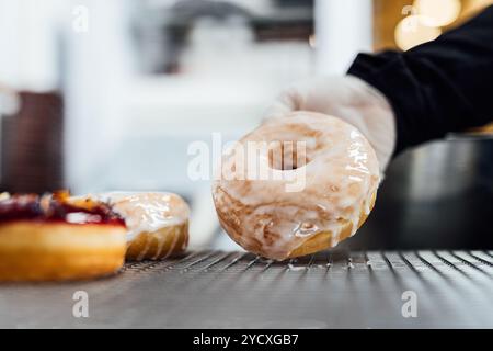 A close-up of a freshly glazed vegan donut being placed on a cooling rack by a baker wearing a glove The smooth, shiny glaze reflects the light, makin Stock Photo
