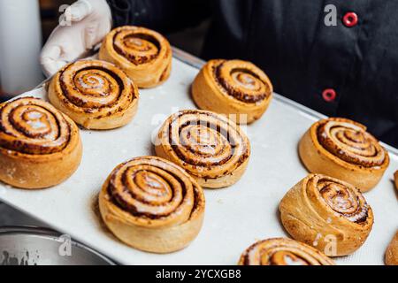 Close-up of freshly baked cinnamon rolls with a rich and savory filling, displayed on a kitchen tray The rolls are topped with a light sugary glaze, e Stock Photo